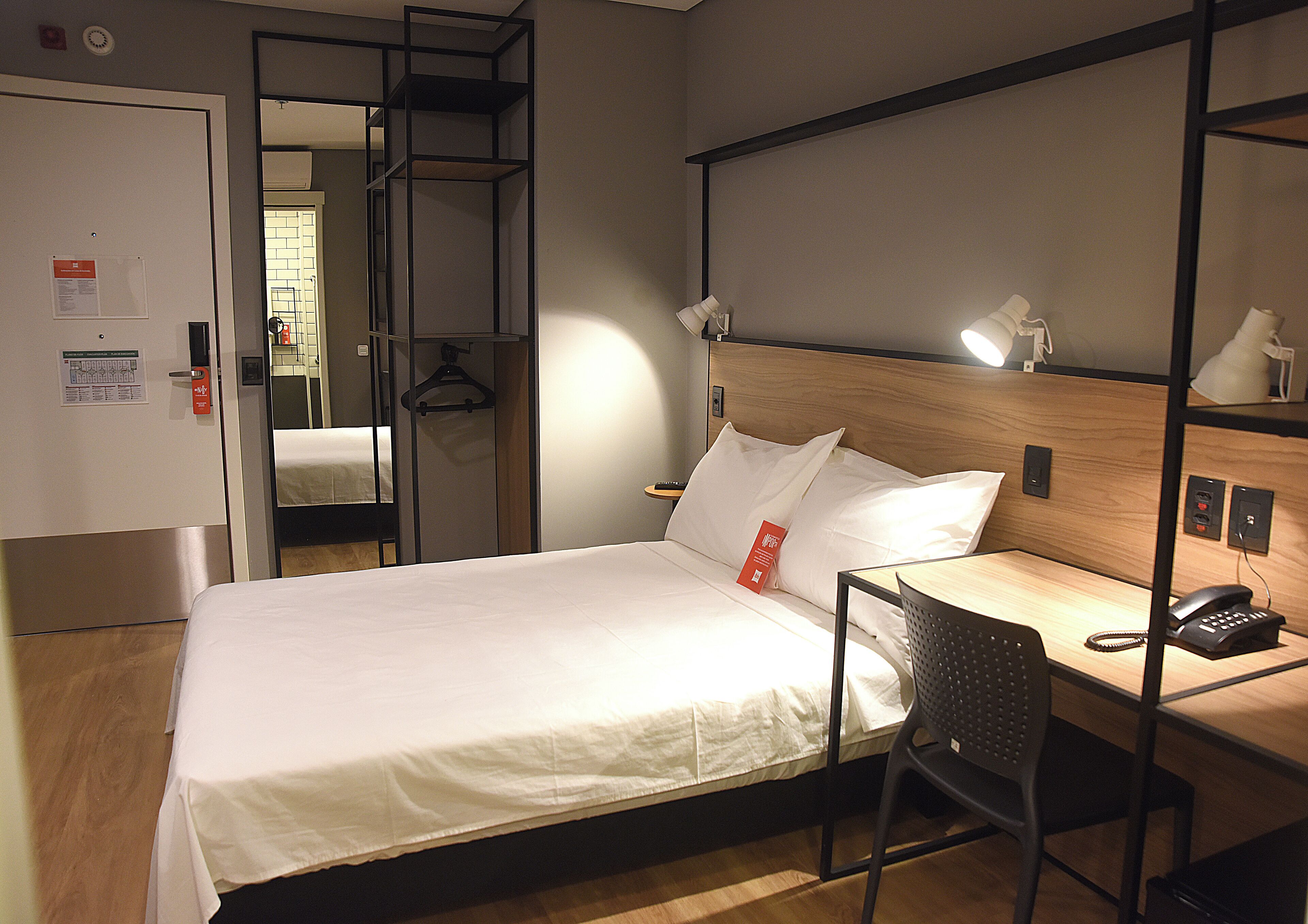 A hotel room with a bed, a desk with a chair, a telephone, and a mirror.