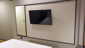 Una habitación de hotel con cama, un espejo grande y un televisor de pantalla plana montado en la pared.