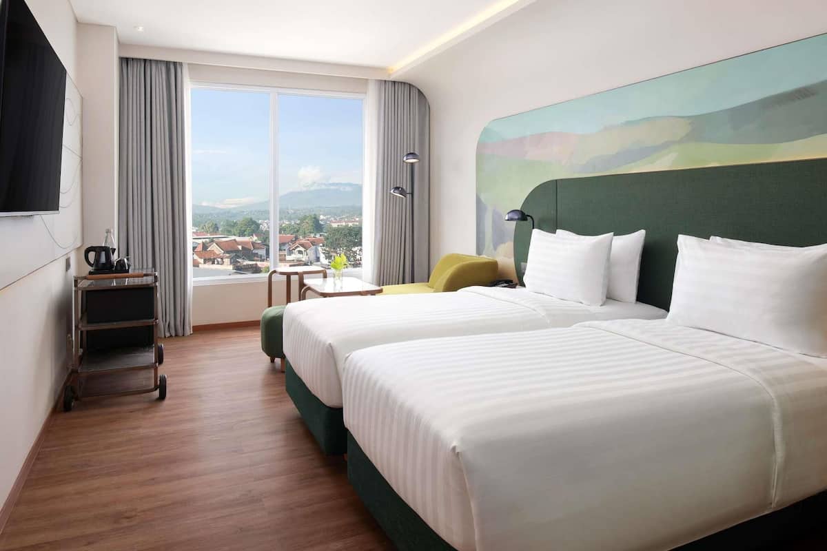 Habitación de hotel con dos camas, televisión, escritorio y vistas a la ciudad.