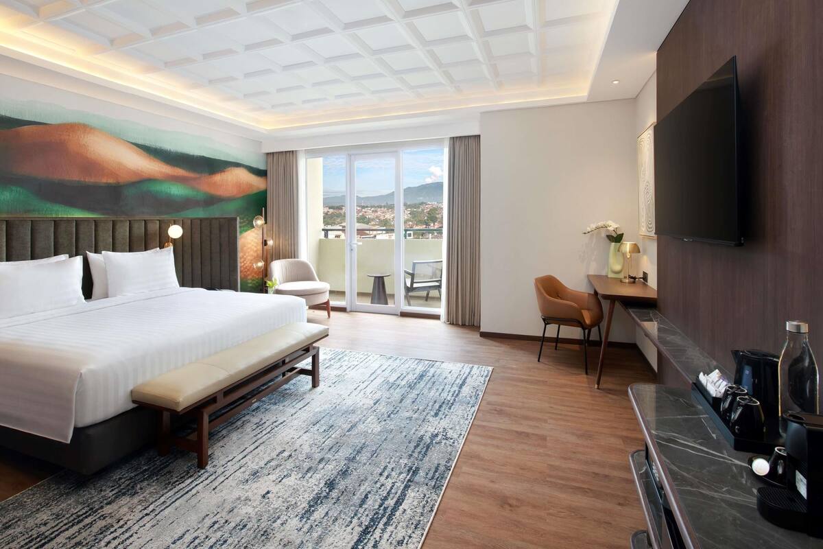 A hotel room with a bed, a desk, a chair, a TV, and a view of the city.