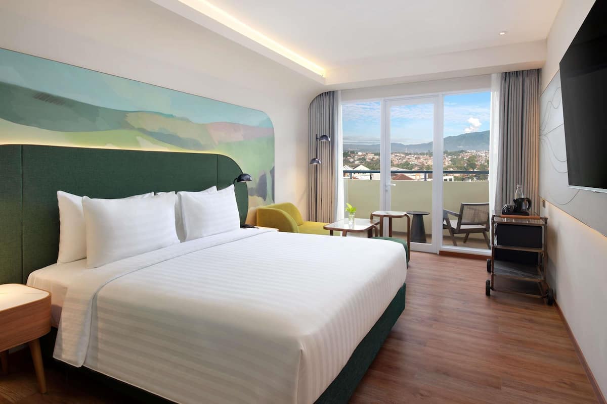 A hotel room with a large bed, a small table, a chair, a TV, and a balcony with a view.
