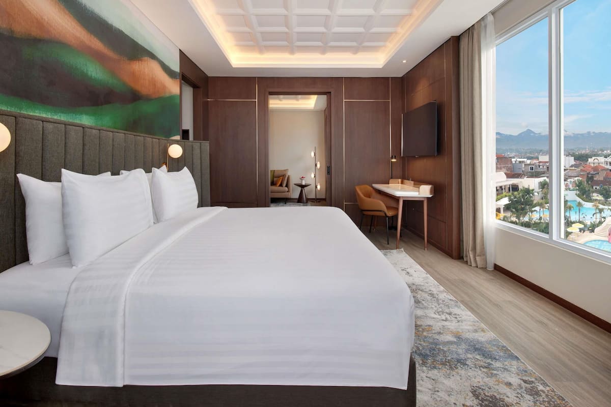 A modern hotel room with a large bed, a desk, and a view of the city.