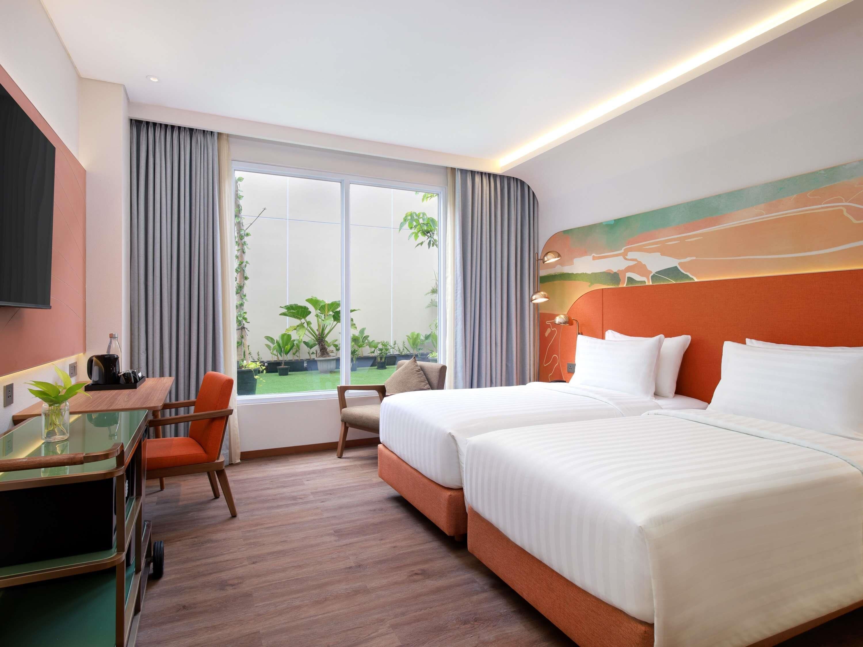 A hotel room with a bed, a desk with a chair, a TV, and a large window with curtains.