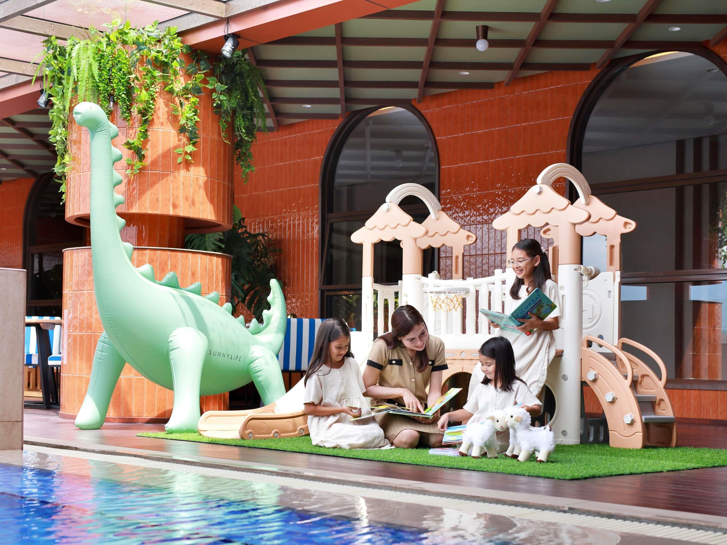 A children's play area with a dinosaur sculpture, a slide, and a reading nook with children and sheep toys.