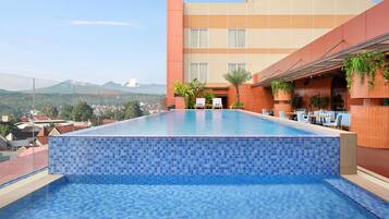 A rooftop infinity pool with a view of distant mountains, a terrace with seating, and a building with a tiled facade.