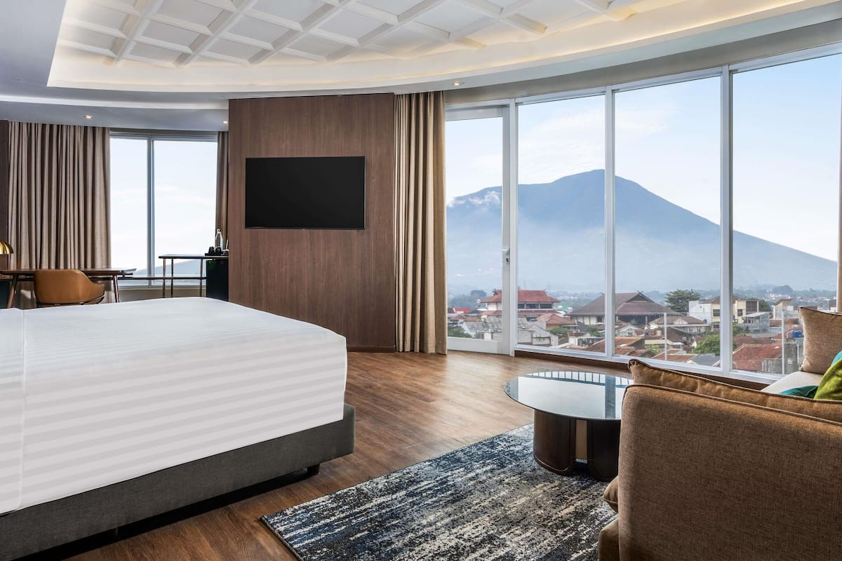 A hotel room with a large bed, a desk, a chair, a TV, and a view of a mountain.