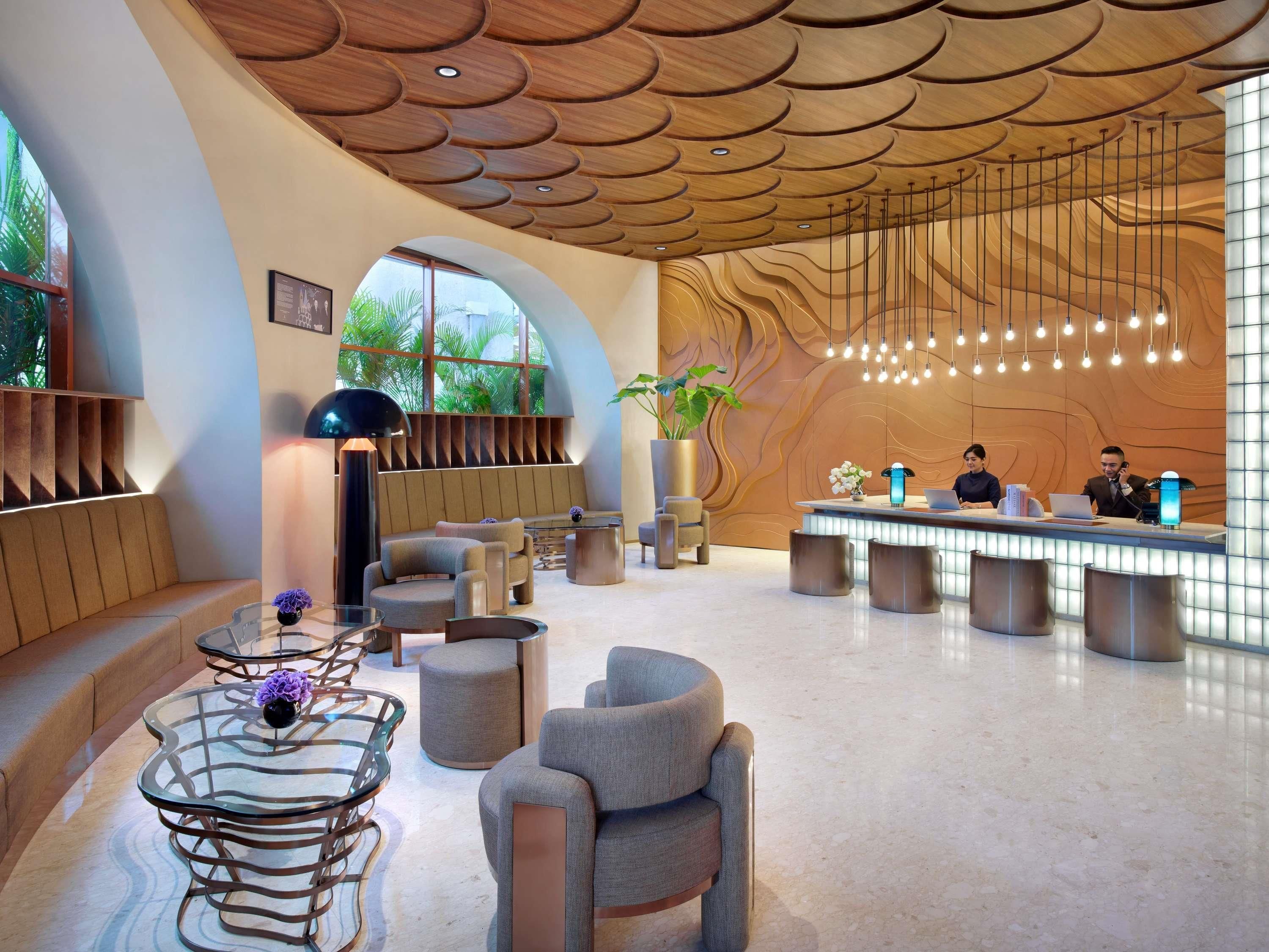Eine moderne Hotelhalle mit gewölbter Decke, Sitzgelegenheiten, einer Rezeption und großen Fenstern.