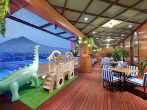 A restaurant with a wooden deck, blue-striped chairs, and a view of a mountain. - Mercure Garut City Center (Garut)