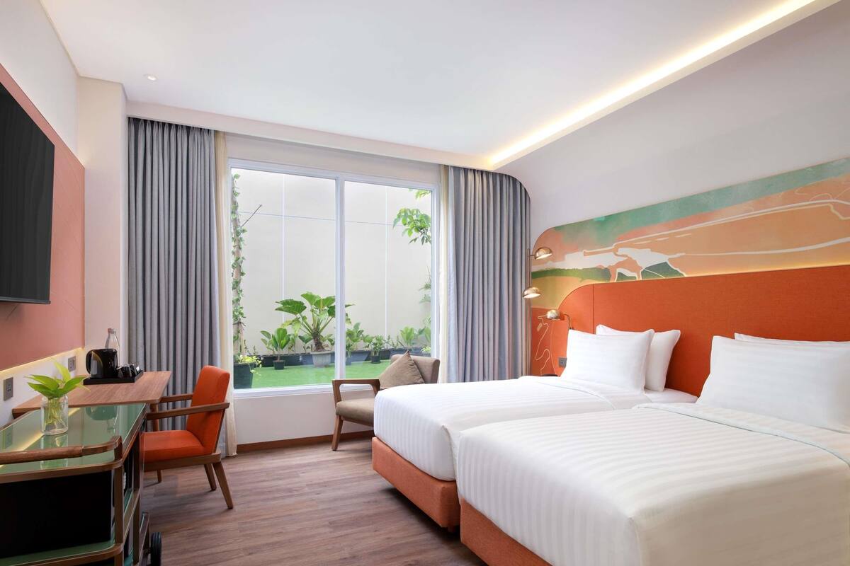 A hotel room with a bed, a desk with a chair, a TV, and a window with curtains.