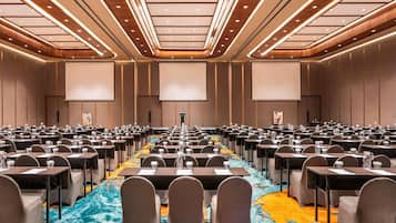 Ein Konferenzraum mit Tischen und Stühlen, einer großen Leinwand im Vordergrund und einem farbenfrohen Teppich.
