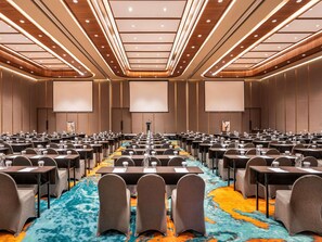 A conference room with rows of tables and chairs, a large screen at the front, and a colorful carpet.