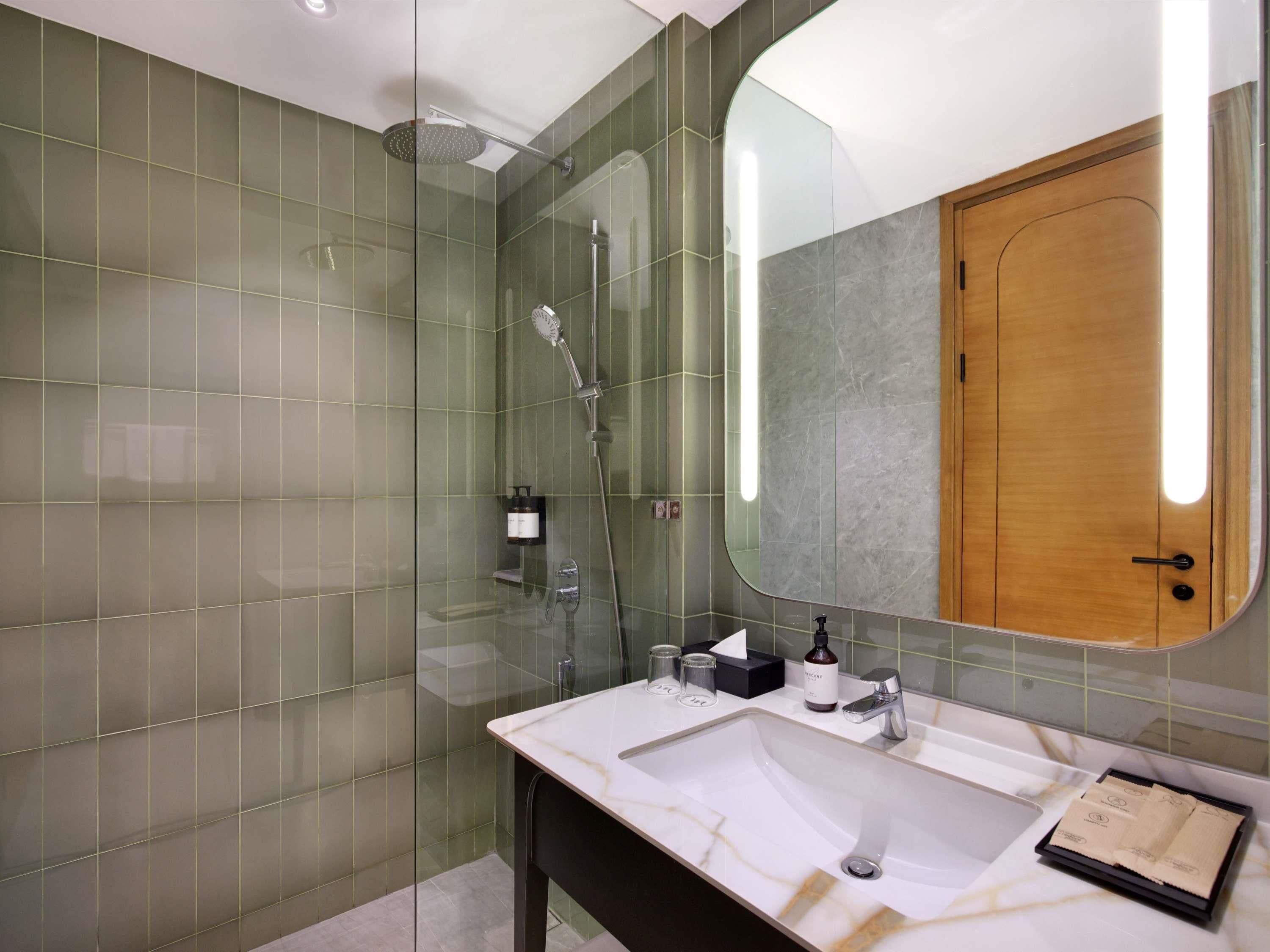 A modern bathroom with a glass-enclosed shower, a marble sink, and a wooden door.