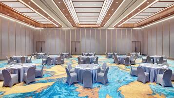 A large conference room with round tables and chairs, a patterned carpet, and a high ceiling with recessed lighting.