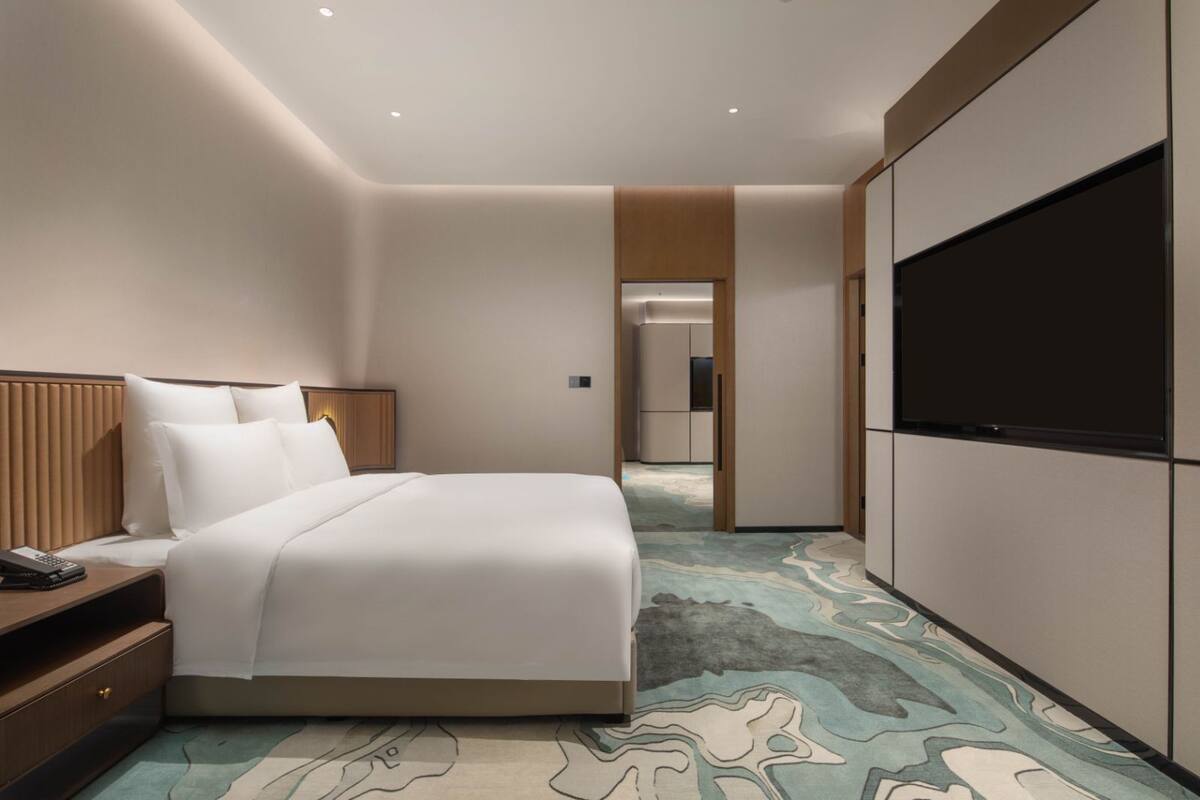 Ein Hotelzimmer mit Bett, Nachttisch, Fernseher und einem gemusterten Teppich.