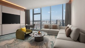 A modern hotel room with a large window offering a city view, a flat-screen TV, a sofa, a chair, and a coffee table. - Novotel Lianyungang Haizhou (Lianyungang)