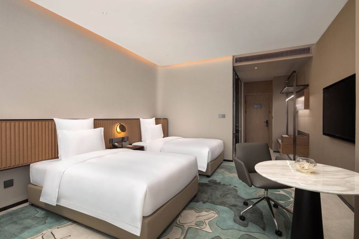 Ein Hotelzimmer mit zwei Betten, einem Schreibtisch, einem Stuhl, einem Fernseher und einer Badezimmertür.