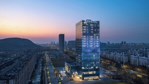 A modern hotel with a prominent 'NOVOTEL' sign, surrounded by urban buildings and a clear sky. - Novotel Lianyungang Haizhou (Lianyungang)