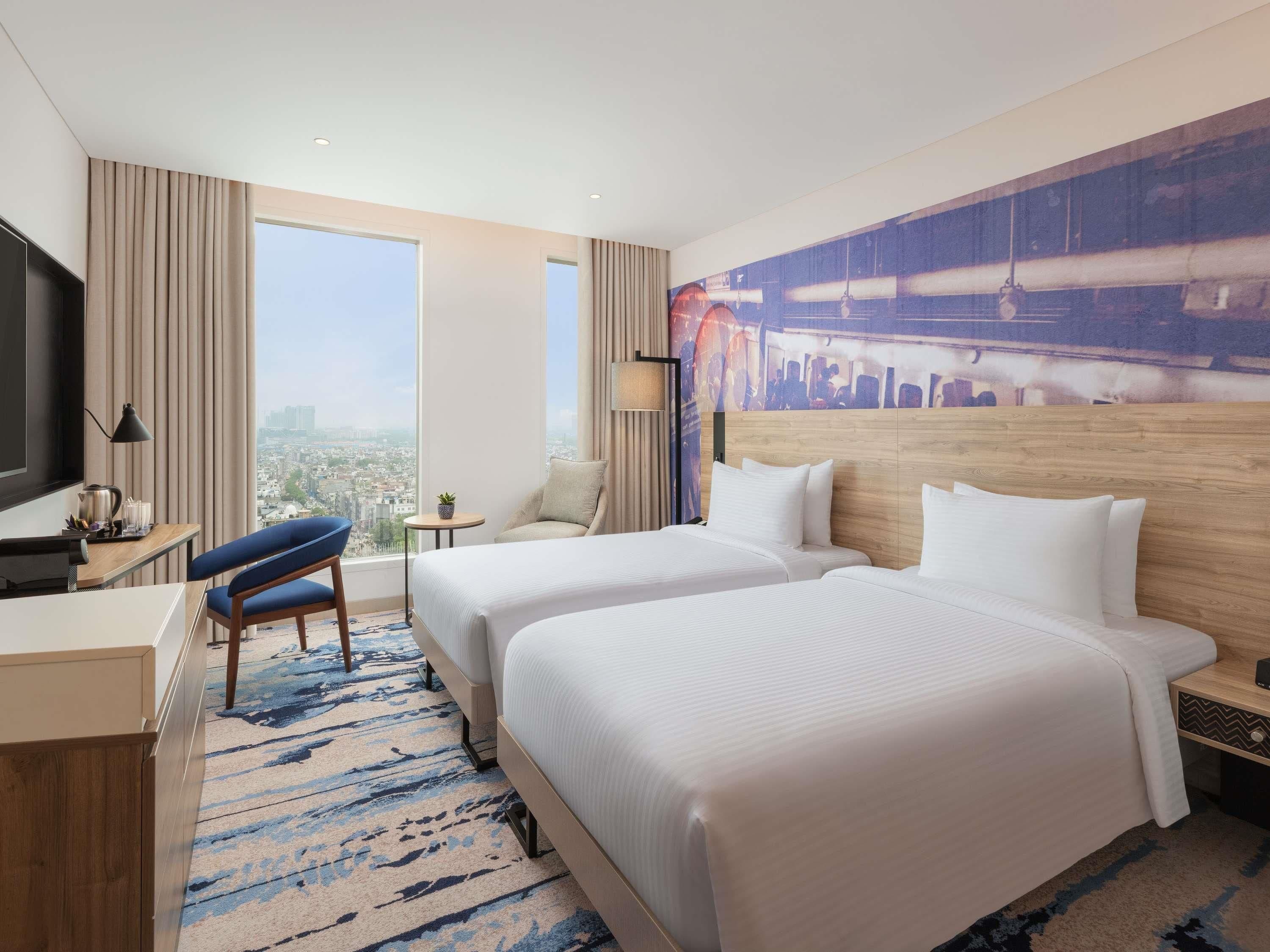 A hotel room with two beds, a desk, a chair, a TV, and a city view.