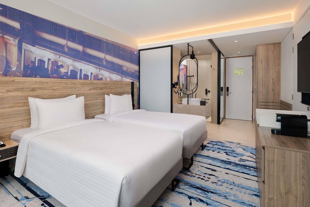 A hotel room with two beds, a large artwork on the wall, a modern bathroom, and a flat-screen TV.