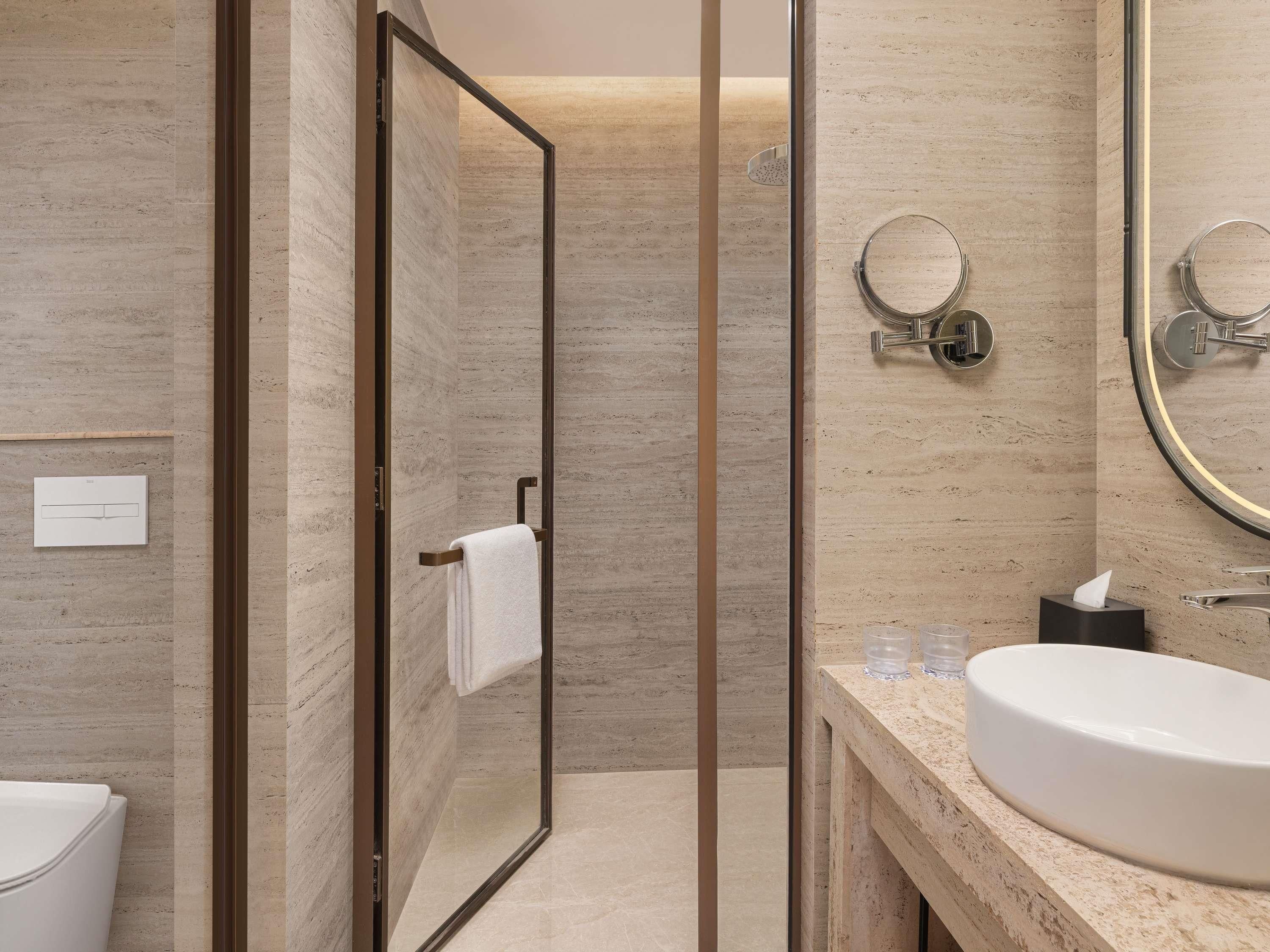 A modern bathroom with a glass shower enclosure, a marble vanity, and a large mirror.