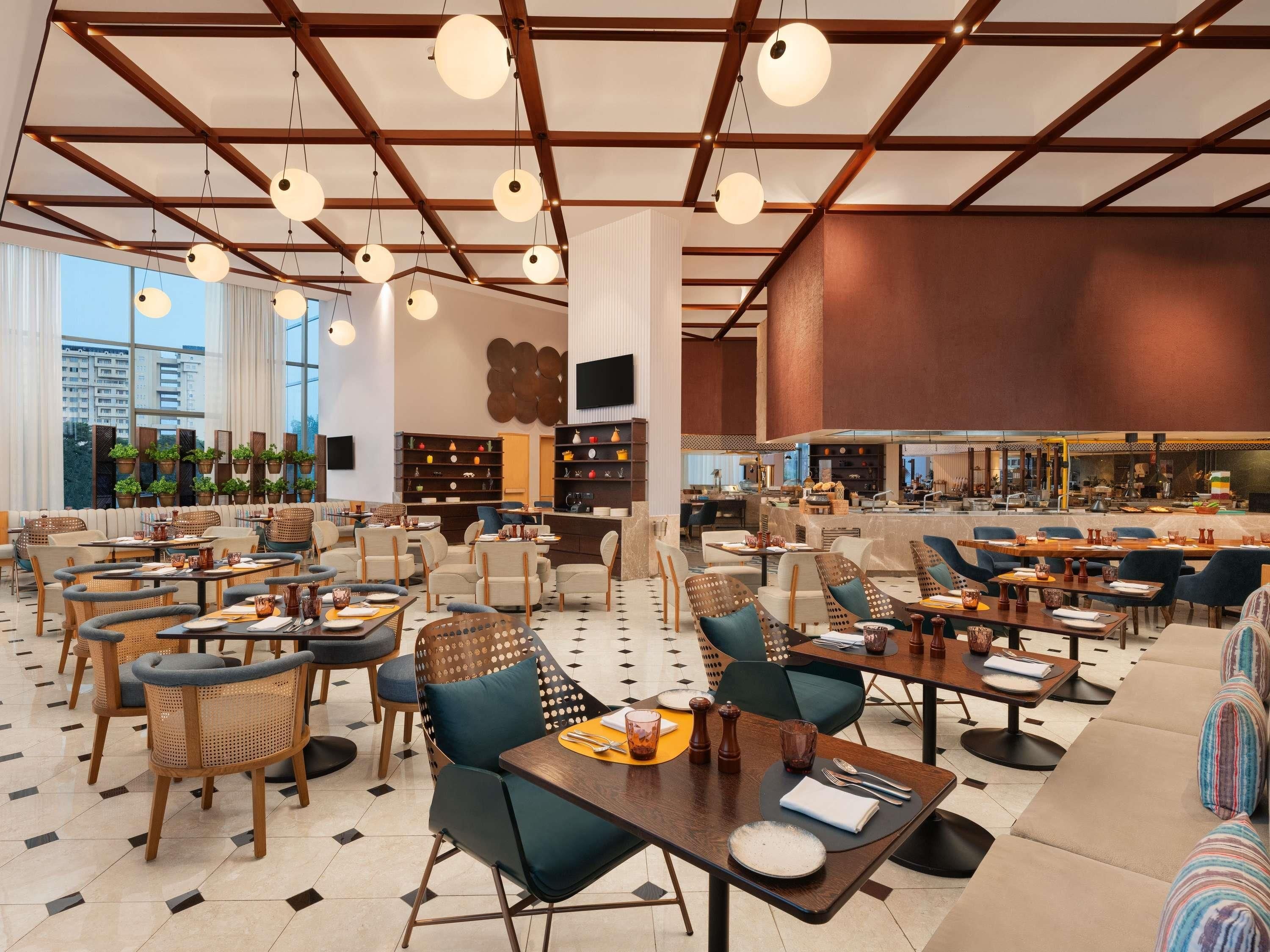 A spacious cafe with multiple seating areas, including tables and chairs, and a visible kitchen area in the background.