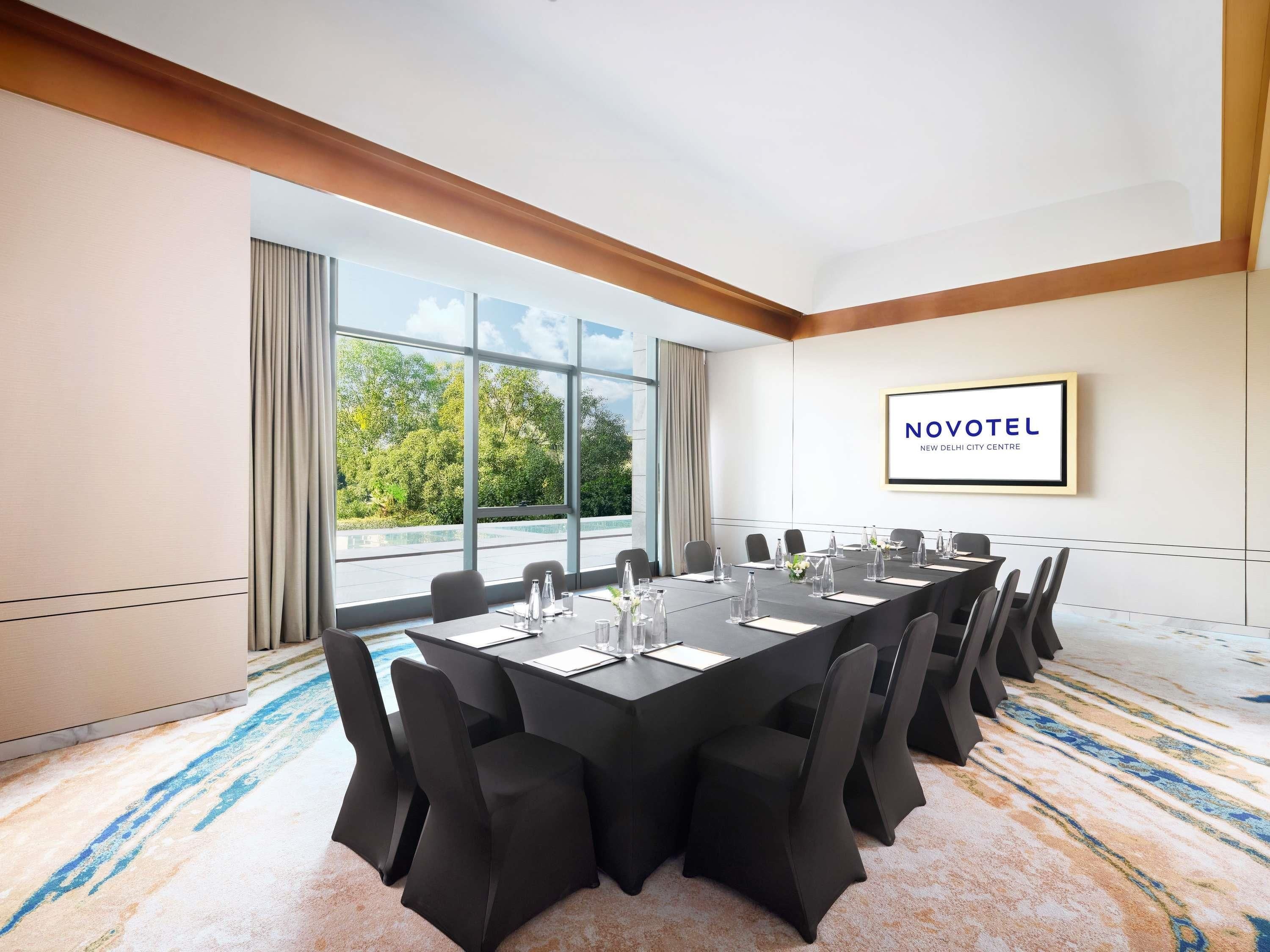 A conference room with a long table, chairs, and a view of trees through large windows.