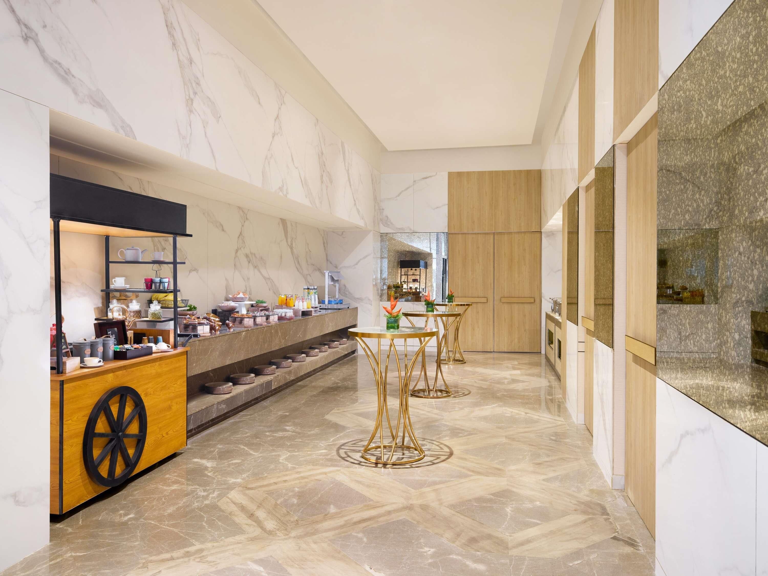A modern interior with marble walls, a buffet counter, and a seating area with gold tables.