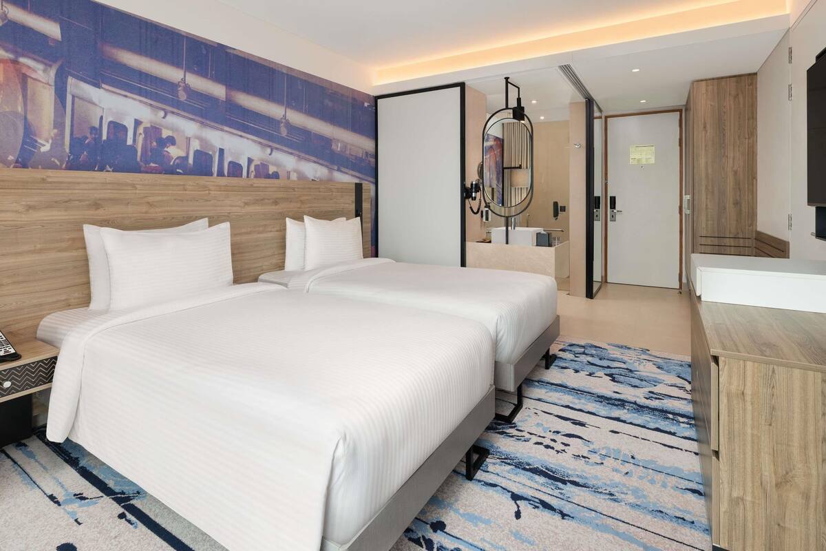 A hotel room with a large bed, a mirror, a wooden headboard, a desk, and a cityscape mural on the wall.