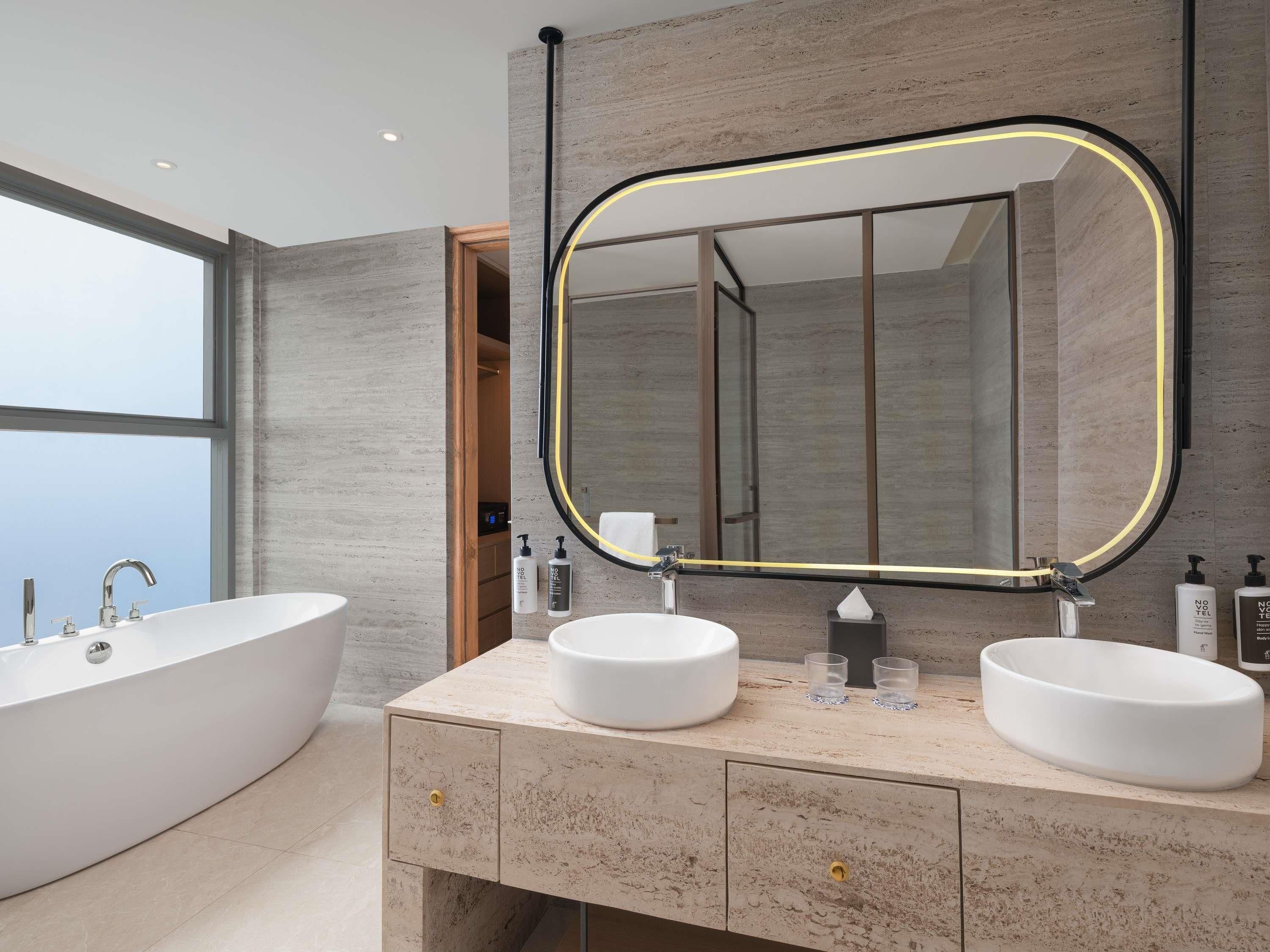 A modern bathroom with a freestanding bathtub, two sinks, a large mirror with a black frame, and a wooden vanity.