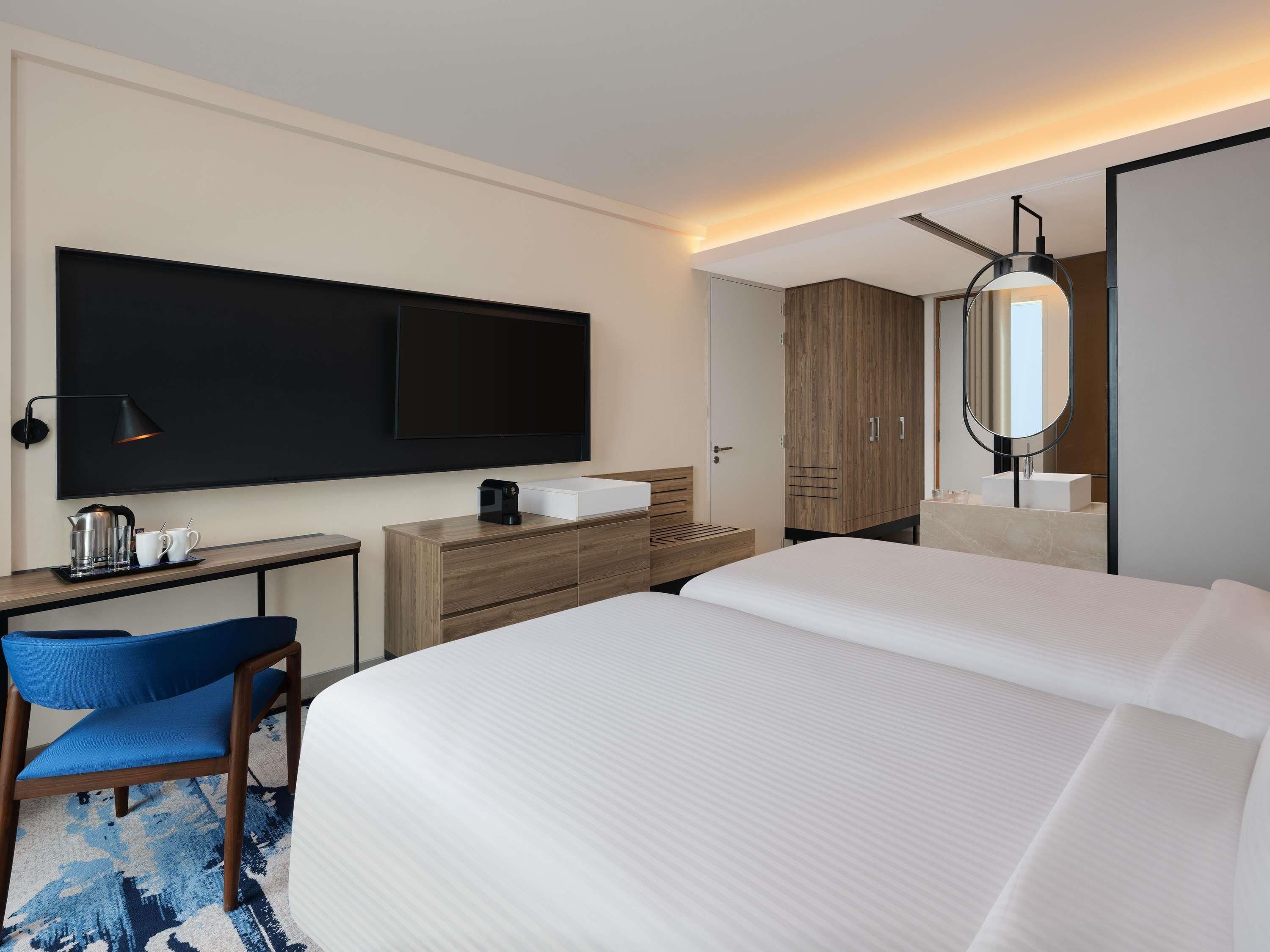A hotel room with a bed, a desk, a chair, a television, a wardrobe, and a bathroom with a mirror.