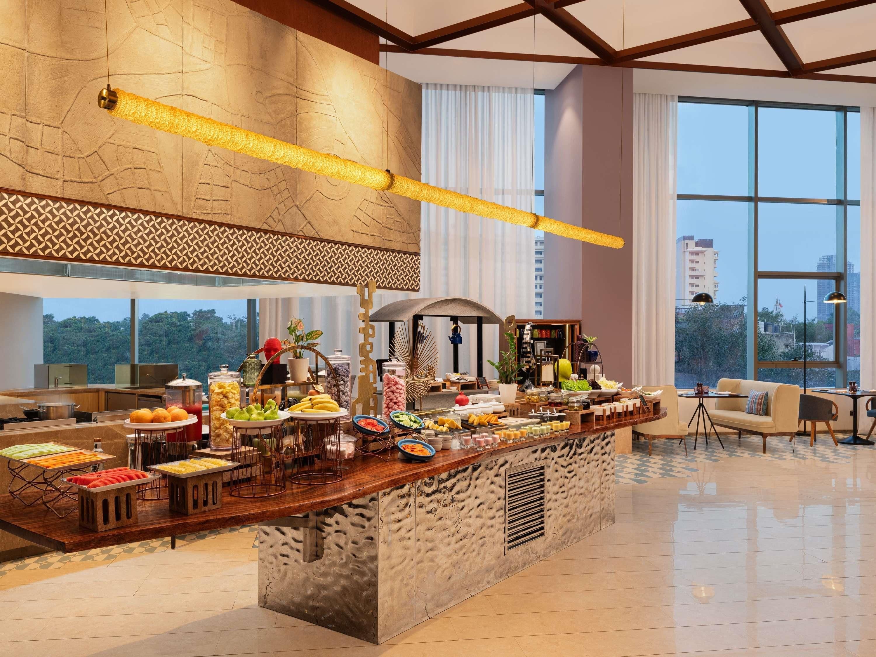 A modern hotel lobby with a buffet area featuring a variety of food items and a seating area with a sofa and chairs.