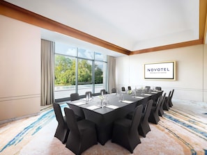 A conference room with a long table, chairs, and a view of trees through large windows.
