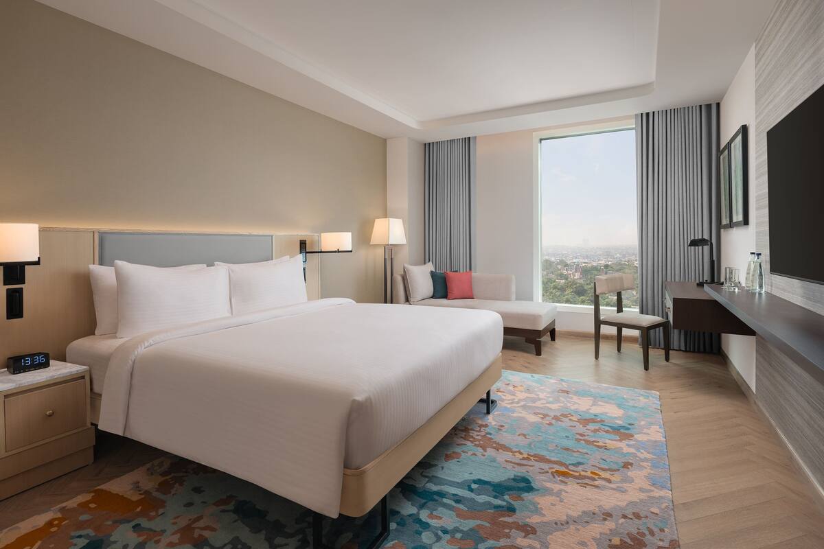 A hotel room with a large bed, a desk, a chair, and a view of the city.