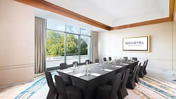 A conference room with a long table, chairs, and a view of trees through large windows.