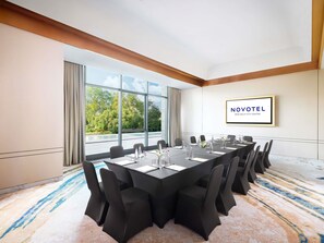 A conference room with a long table, chairs, and a view of trees through large windows. - Novotel New Delhi City Centre (New Delhi)