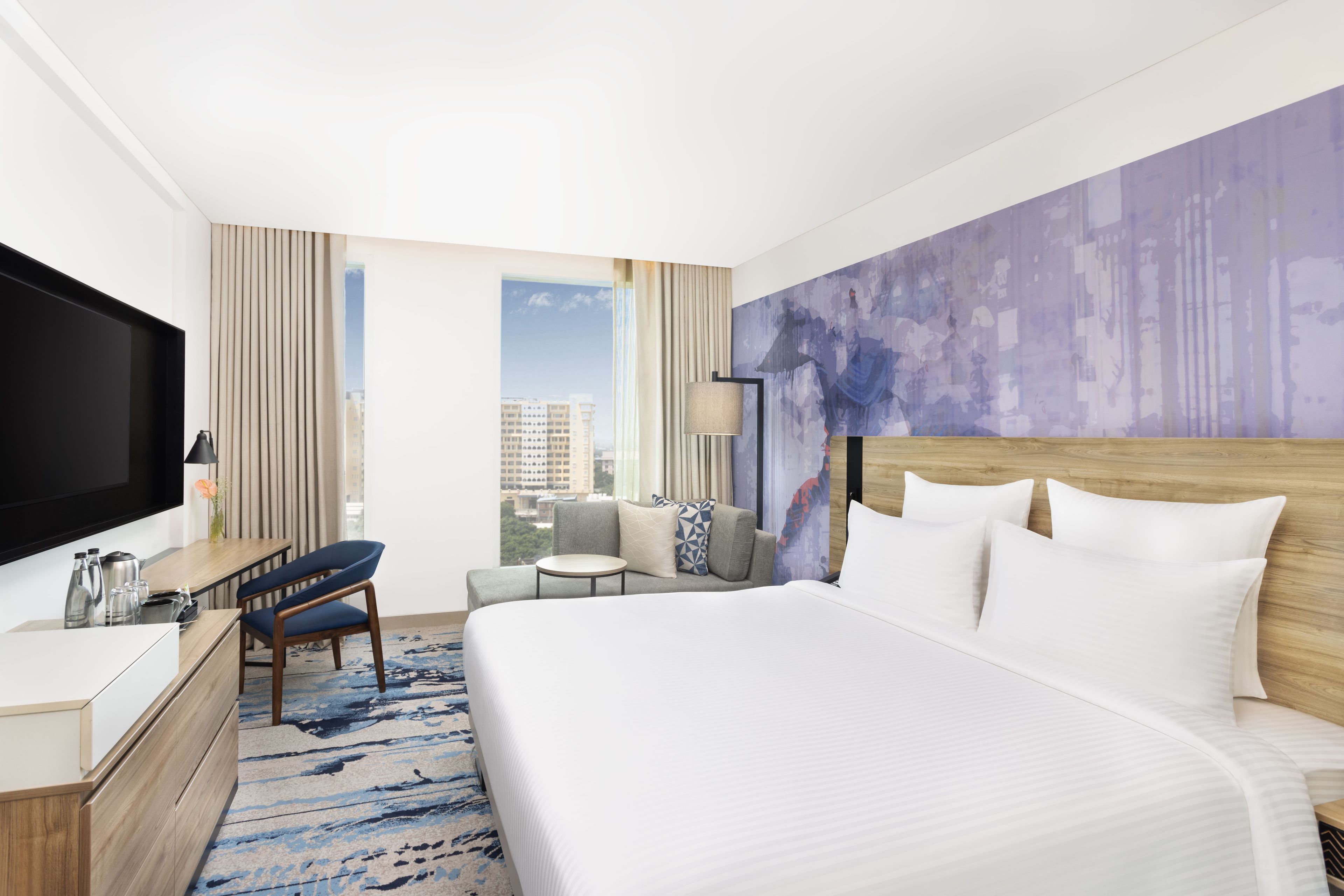Habitación de hotel con una cama grande, un escritorio con televisor de pantalla plana, un sofá y vista a la ciudad.