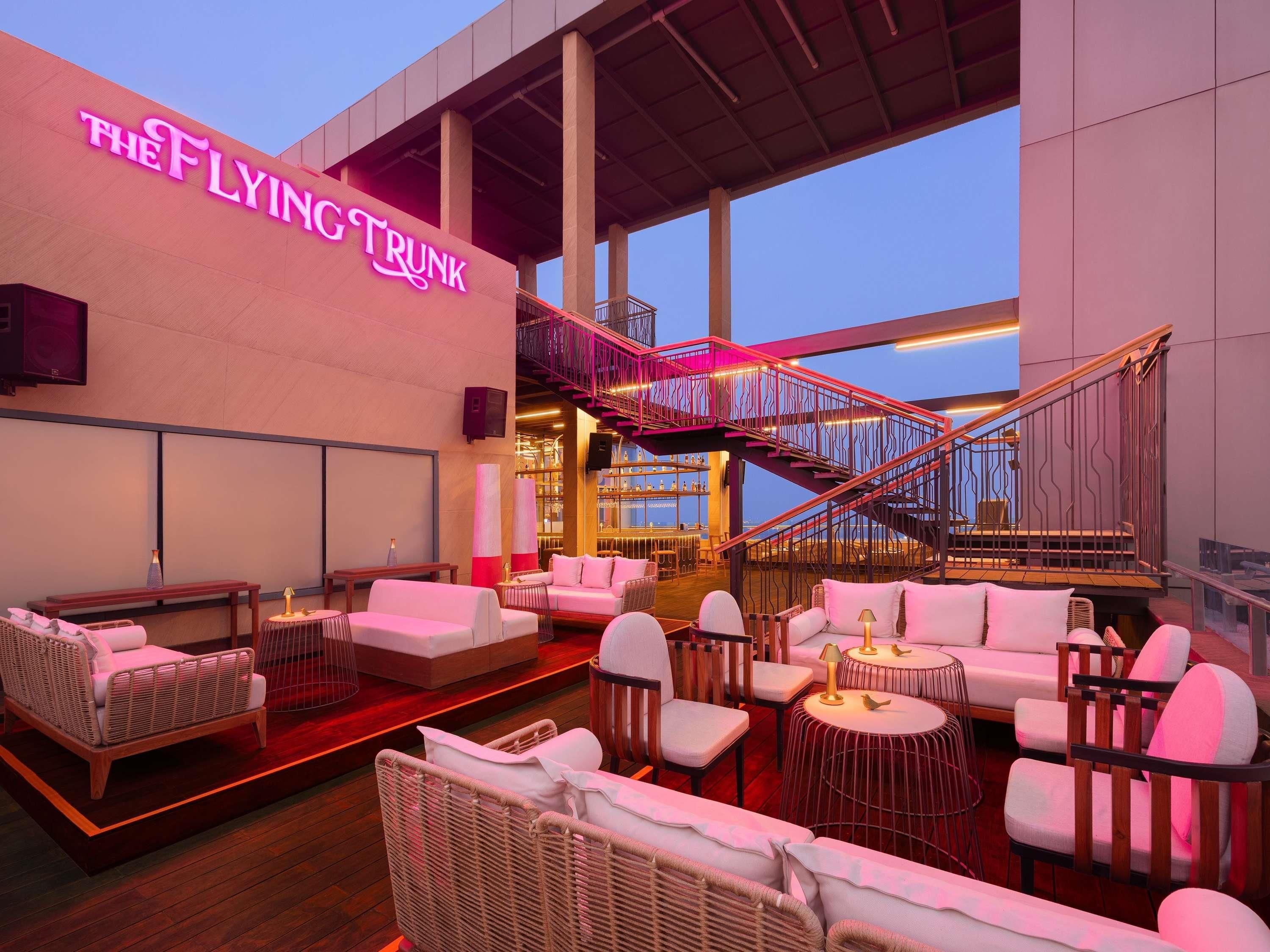 A modern hotel lobby with a staircase, seating areas, and a neon sign.