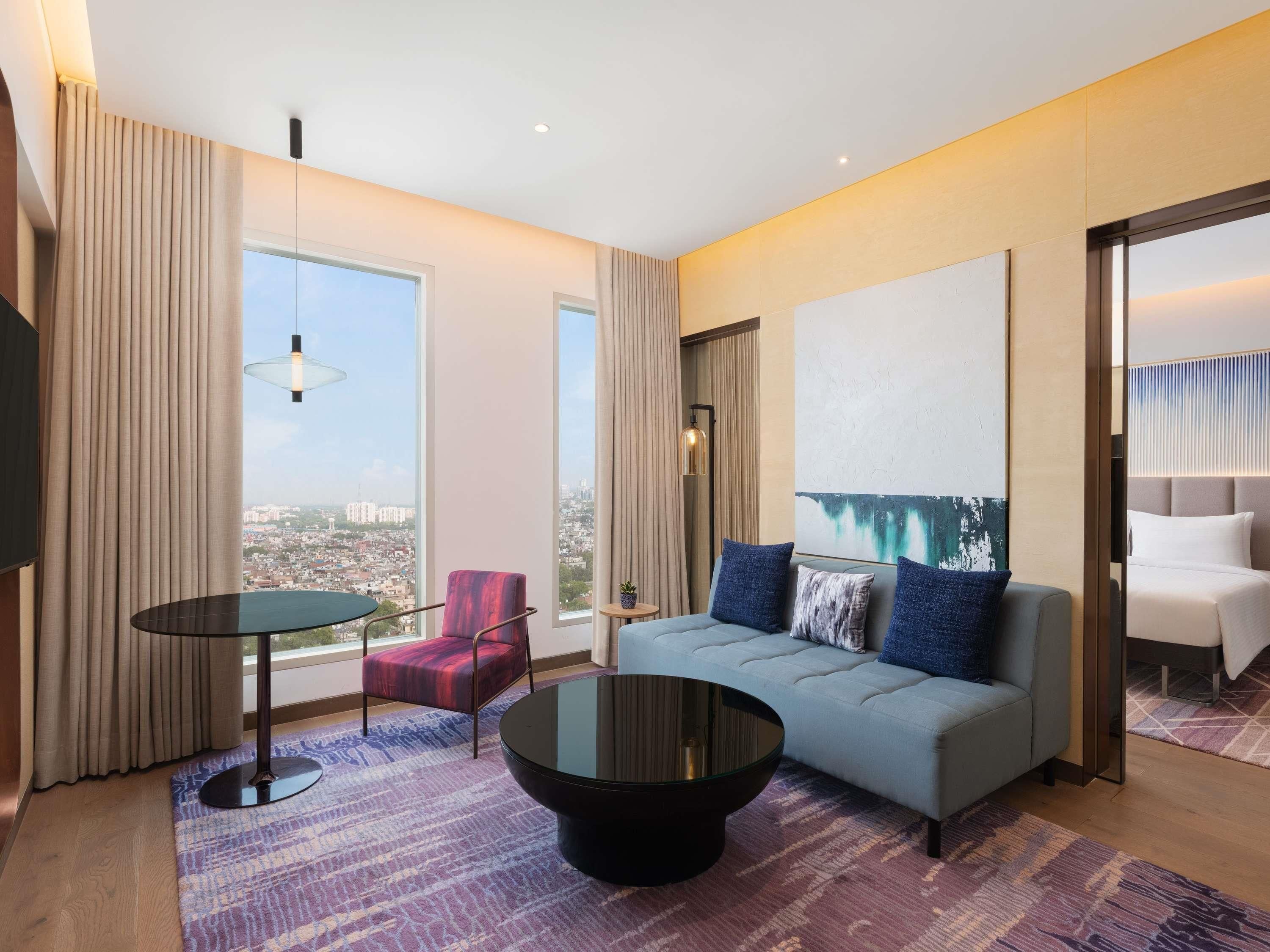 A modern hotel room with a large window, a sofa, a coffee table, and a chair.
