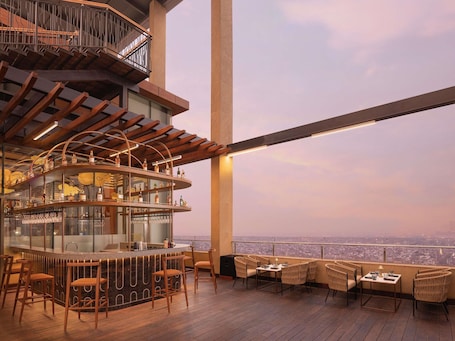 A bar area with a panoramic city view, wooden flooring, and a high ceiling.