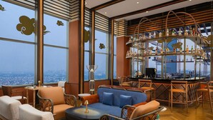 Un bar en un rascacielos con vistas panorámicas de la ciudad, que cuenta con mobiliario moderno y una zona de bar central.