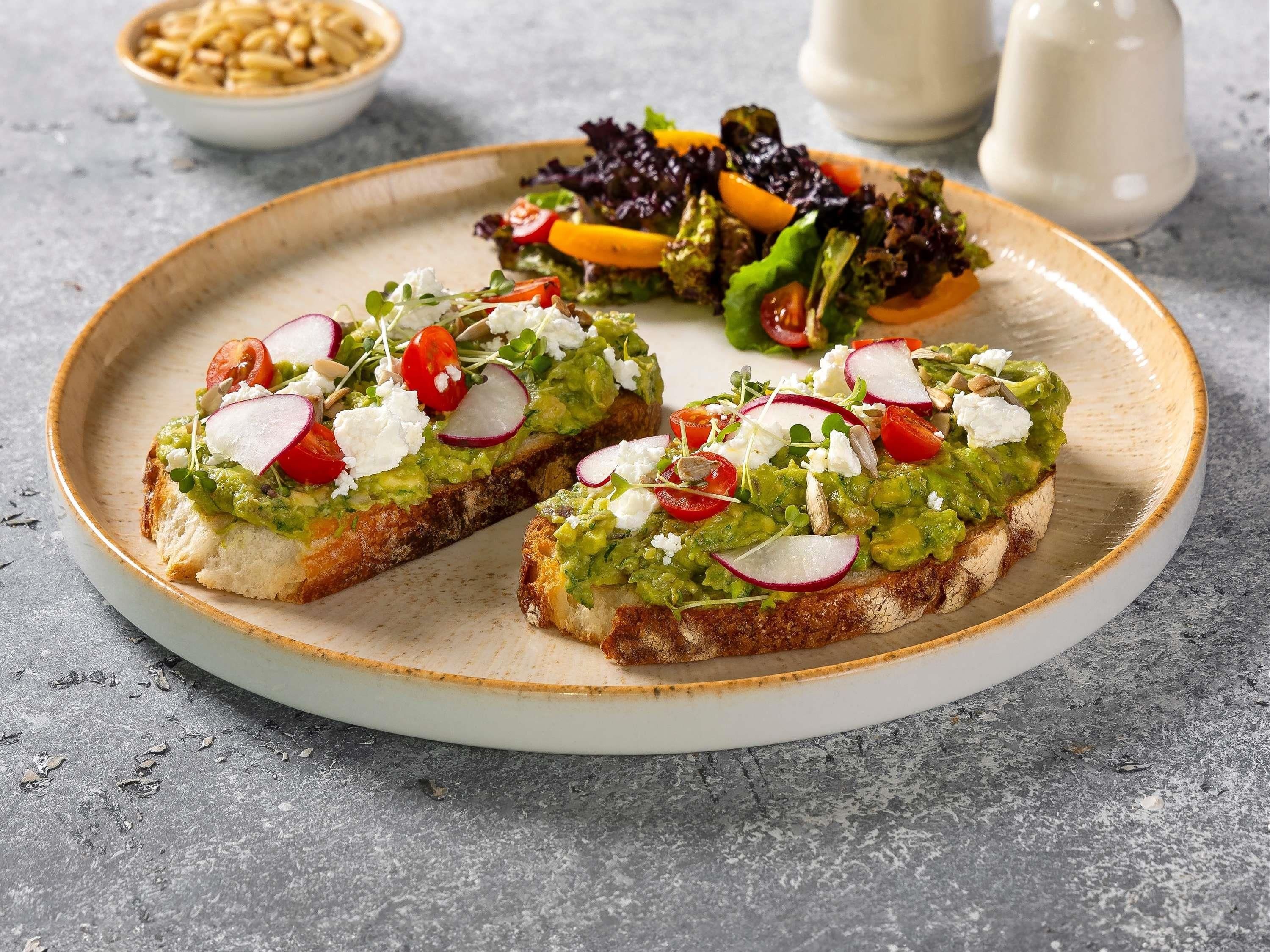 A plate with avocado toast garnished with radishes and tomatoes, and a side salad.