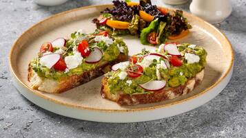 Une assiette de pain grillé garni d’avocat, accompagné de radis et de tomates, et une salade en accompagnement.