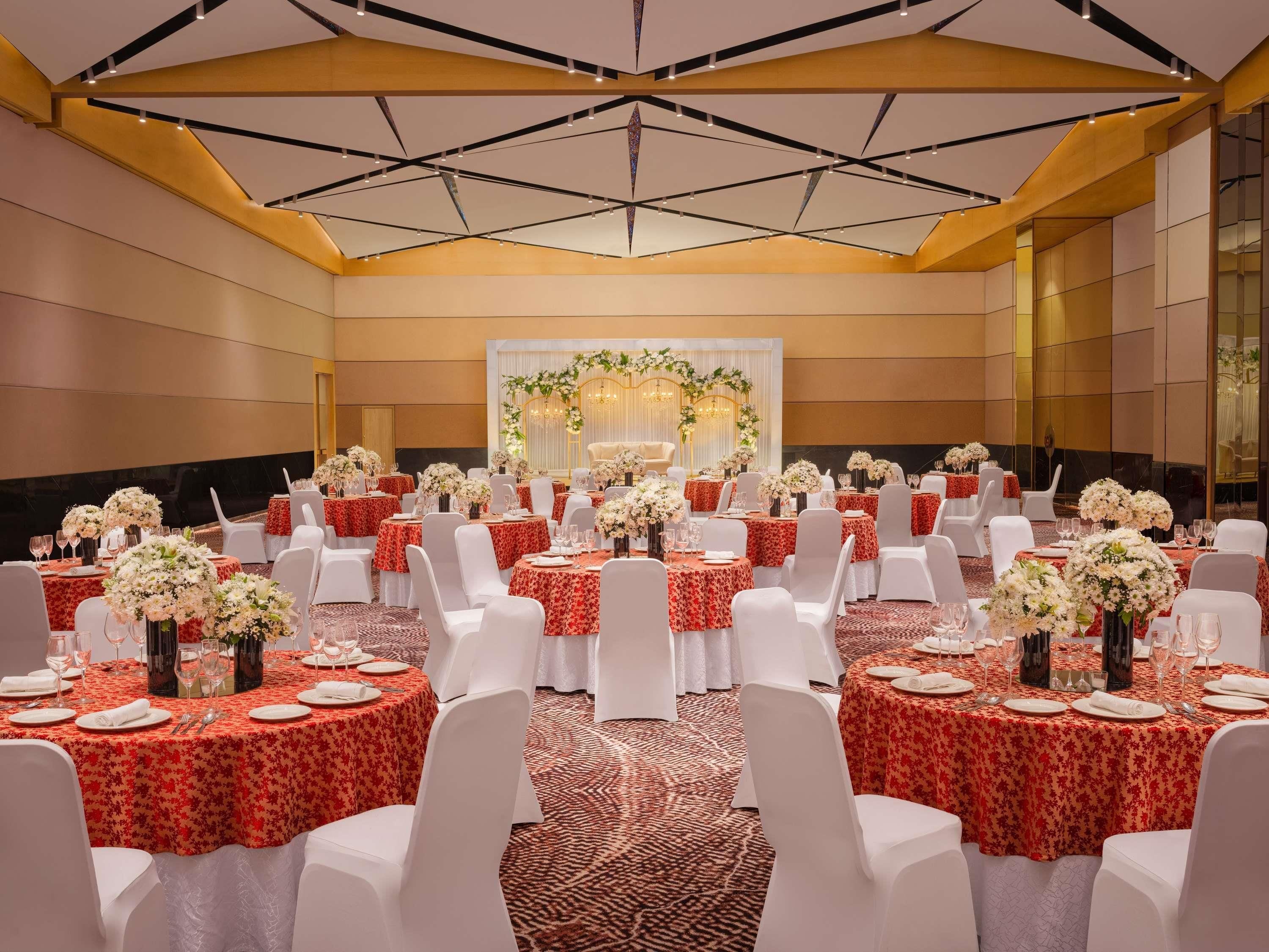 Une salle de banquet avec des tables rondes, des chaises blanches et des centres de table ornés de compositions florales.
