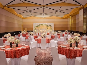 A banquet hall with round tables, white chairs, and floral centerpieces.