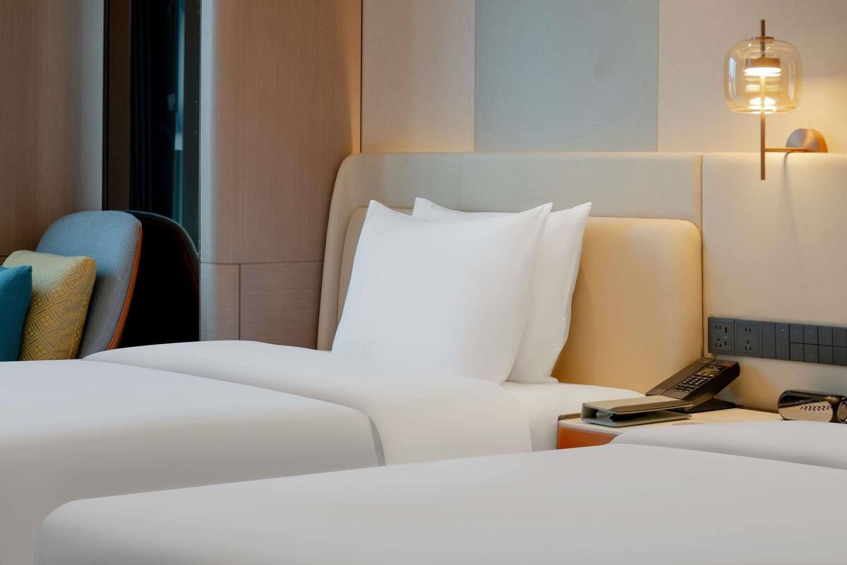Una habitació d'hotel amb un llit, una cadira, una taula de nit, una làmpada i un telèfon fixat a la paret.