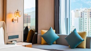 A modern hotel room with a sofa, pillows, a wall-mounted light fixture, and a window with a city view. - Pullman Renhuai Chuangmeng (Zunyi)