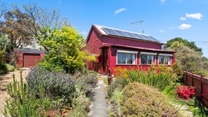 A red house with solar panels, a garden with various plants, and a clear blue sky.