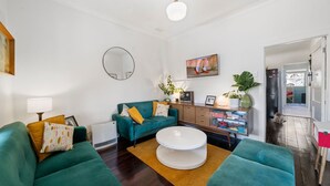 A modern living room with teal sofas, a white coffee table, and a wooden cabinet with books and decorative items.