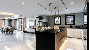 A modern kitchen with a central island, pendant lighting, and a dining area with a table and chairs. - EDEN'S Homes & Villas - Balqis Residence (Dubai)