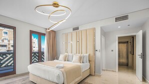 A modern hotel room with a large bed, a view through a balcony door, and a contemporary light fixture. - EDEN'S Homes & Villas - Balqis Residence (Dubai)